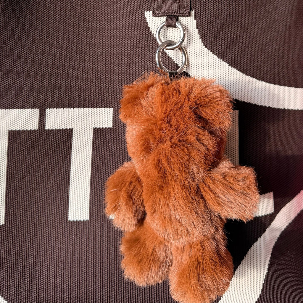 UTTAL Chestnut Plushy Teddy Bag Charm attached to a brown knitted tote bag